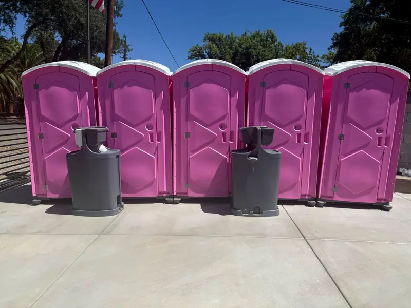 Five pink porta potties with two handwash stations on a paved lot